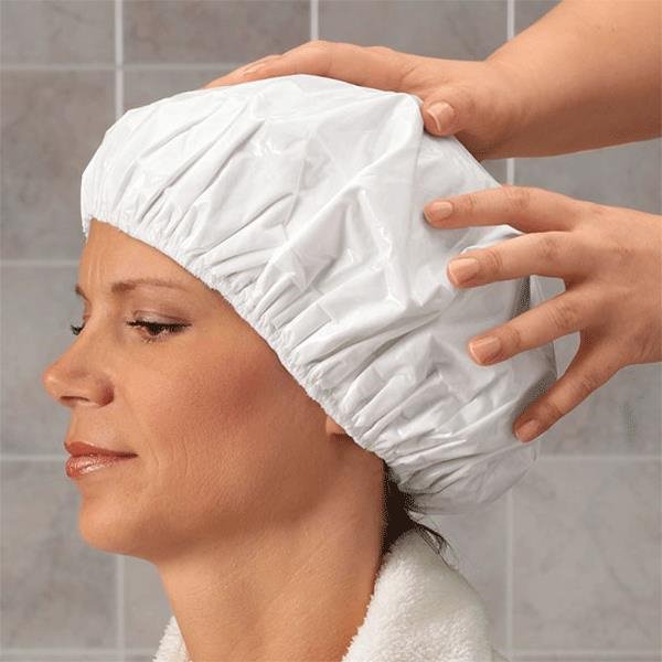 woman with a white shampoo cap on while a caregiver is performing the care