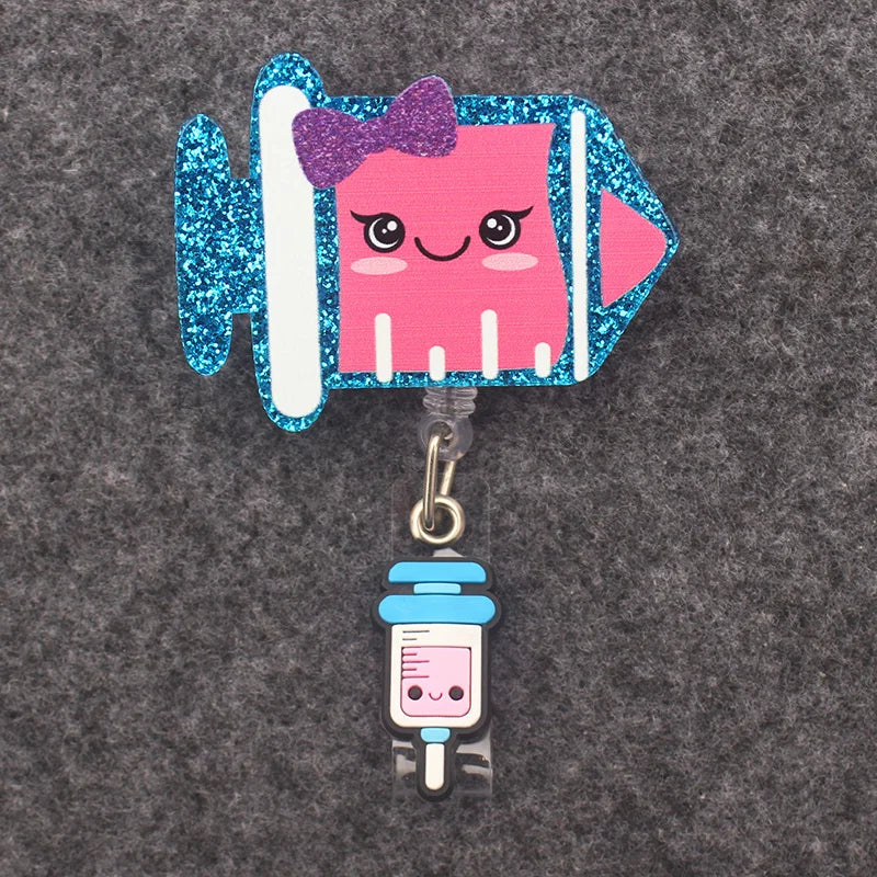 badge reel - glittery syringe with a smiley emoji face with a bow. Under ID holder clasp, a white/blue syringe.