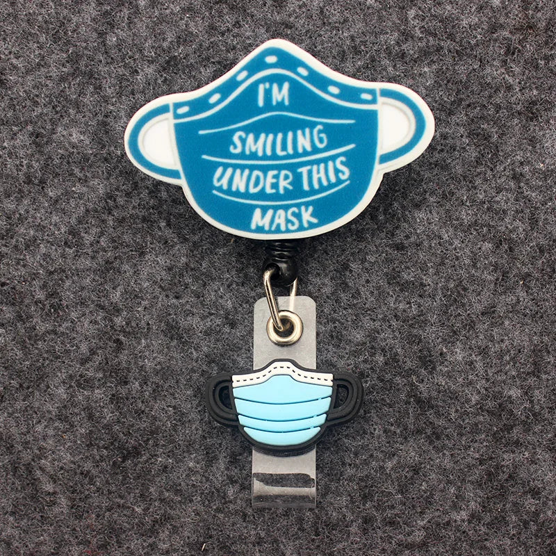 badge reel "I'M SMILING UNDER THIS MASK". Under ID holder clasp, a blue mask.